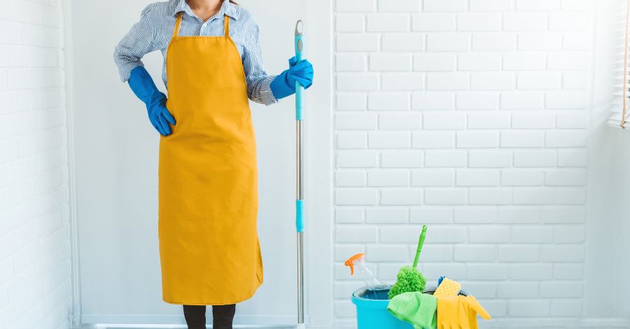 Woman (cut off at neck) holiding a mop with janatorial supplies on the floor beside her
